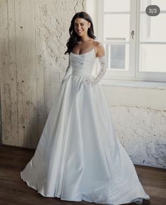 a woman in a white wedding dress standing next to a window with her hands on her hips