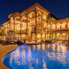 a large mansion with a swimming pool in front of it at night, surrounded by palm trees