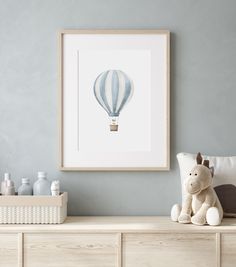 a white teddy bear sitting on top of a dresser next to a framed hot air balloon