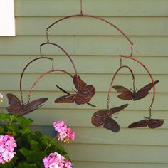 a wind chime hanging from the side of a house with pink flowers in front of it