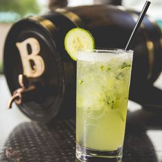 a drink with cucumber and mint on the rim next to a black clock