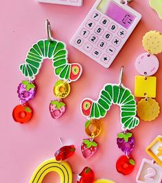 some very pretty colorful earrings on a pink surface with a calculator and cell phone