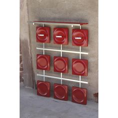 red plates are arranged on a metal rack in front of a concrete wall and cement floor