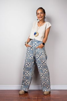 a woman standing in front of a white wall wearing blue patterned pants and a necklace