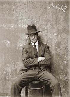 a man in a suit and hat sitting against a wall