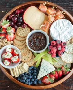 a wooden platter filled with cheese, crackers, fruit and other food items