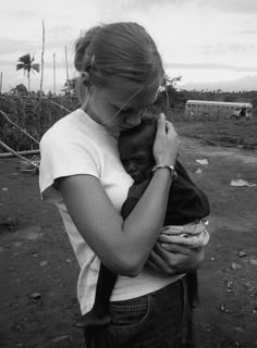 a woman holding a baby in her arms while standing on a dirt field with palm trees