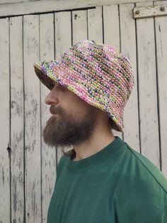 a man with a beard wearing a multicolored knitted bucket hat in front of a wooden wall