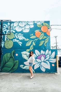 a woman standing in front of a painted wall with flowers and leaves on the side