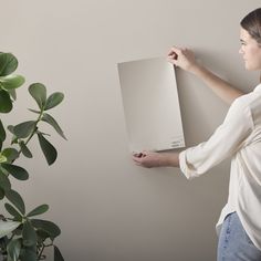 a woman holding up a piece of white paper next to a potted plant on the wall