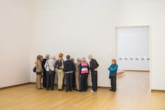 a group of people standing in front of a white wall looking at pictures on the wall