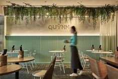 a woman standing in front of a green wall with plants hanging from it's ceiling