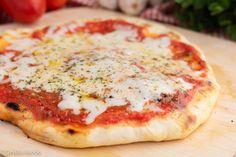 a pizza sitting on top of a wooden cutting board next to tomatoes and garlics