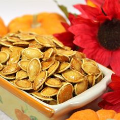 a bowl filled with pumpkin seeds next to flowers