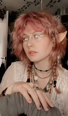 a woman with pink hair and horns on her head, wearing silver rings and necklaces