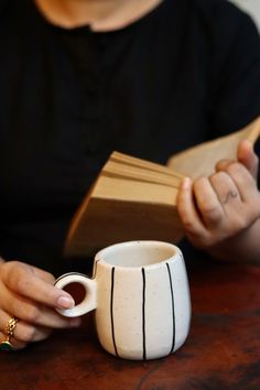 a woman sitting at a table with a book and coffee mug