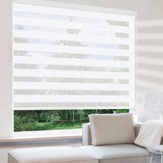 a living room with a white couch and large window covered in vertical blind shades that look out onto the yard