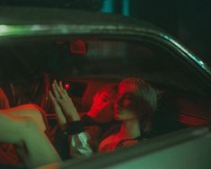 two people sitting in the back seat of a car, one is holding her hand up