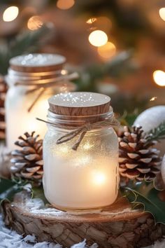 two mason jars filled with candles sitting on top of snow covered ground next to pine cones