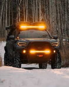 a truck is driving through the snow with its lights on and it's hood up