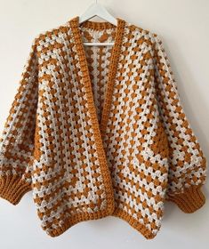 an orange and white crocheted sweater hanging on a hanger