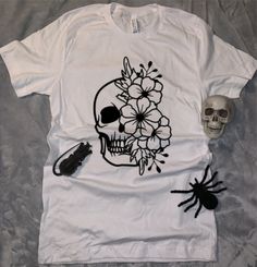 Show your love for Halloween with this floral skull shirt! Shirt comes in a variety of colors/sizes, please choose from the drop down options. Sizes are unisex so they run a little bigger than a fitted shirt. All shirts are specified with the shirt color and vinyl color. *If you are looking for another size, please reach out in a message.* All shirts are made to order and ship in 1-3 business days via USPS. Shirts should be washed inside out, gentle cycle, with cold water. Hang to dry or tumble dry on low. I do not accept returns, however if you have any issues with your order please message me! I hope you enjoy your new tee. Please don't forget to leave a review! Skull T Shirt Design Ideas, Womens Skull Shirts, White T-shirt With Skull Print For Fall, Cotton T-shirt With Custom Skull Print, Cotton T-shirt With Skull Print, Spring Black T-shirt With Skull Print, Skull Shirts, Floral Skull, Skull Tshirt