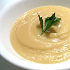 a white bowl filled with yellow soup and garnished with parsley on top