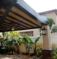 a patio covered in plants and trees next to a building with a roof over it