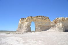 an arch shaped rock formation in the middle of a desert area with blue skies above