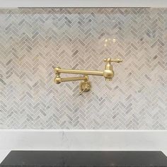 a black counter top under a gold faucet in a white tiled kitchen with herringbone backsplash