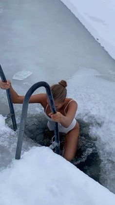 a woman in a white bathing suit sitting on the edge of an icy body of water