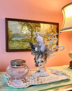 a table topped with a white vase filled with pearls next to a mirror and lamp