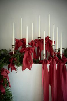 white candles with red bows and greenery in front of wall decorated with evergreen garland