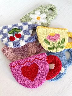 four crocheted tea cups with hearts and flowers on them, all in different colors