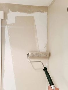 a person is painting the walls with white paint and a green brush in their hand