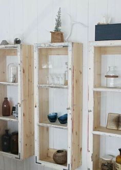 two wooden shelves with glass jars and vases on them in a white walled room