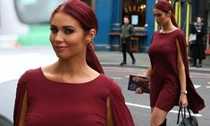 a woman with red hair is walking down the street wearing a maroon dress and carrying a black handbag