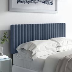 a bed with white sheets and blue headboard next to a painting on the wall