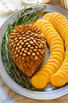 a pine cone and crackers are arranged on a silver plate with green sprigs