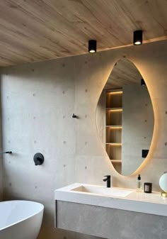 a white bath tub sitting next to a bathroom sink under a large oval shaped mirror