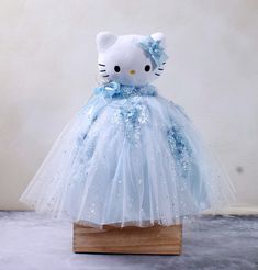 a hello kitty doll in a blue dress on a wooden stand with white walls behind it