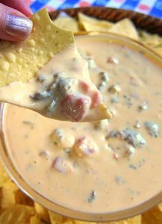 a person holding a tortilla chip and dipping it into a bowl of dip