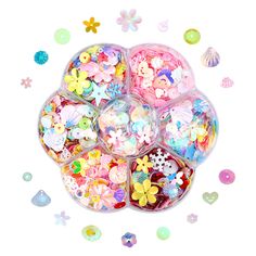 an assortment of buttons in a plastic container with confetti scattered around it on a white background