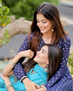 two women sitting next to each other on a bench smiling at each other and hugging