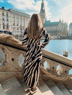 a woman standing on the edge of a railing looking at water and buildings in the background