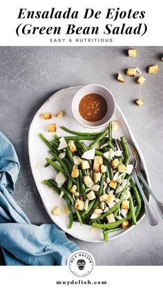 green bean salad on a white plate with a small bowl of sauce and blue napkin