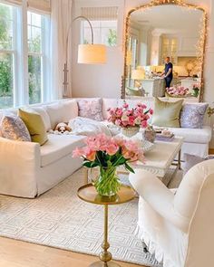 a living room filled with white furniture and lots of pink flowers on top of a table