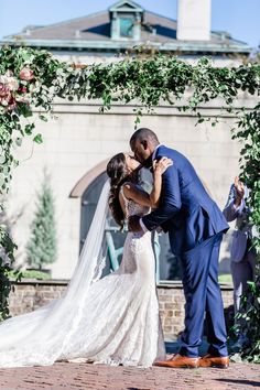 a bride and groom kissing under an arch with greenery