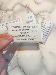 someone is holding up some business cards on a marble counter top with white and pink lettering