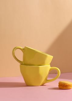 two yellow cups sitting next to each other on top of a pink tablecloth covered floor